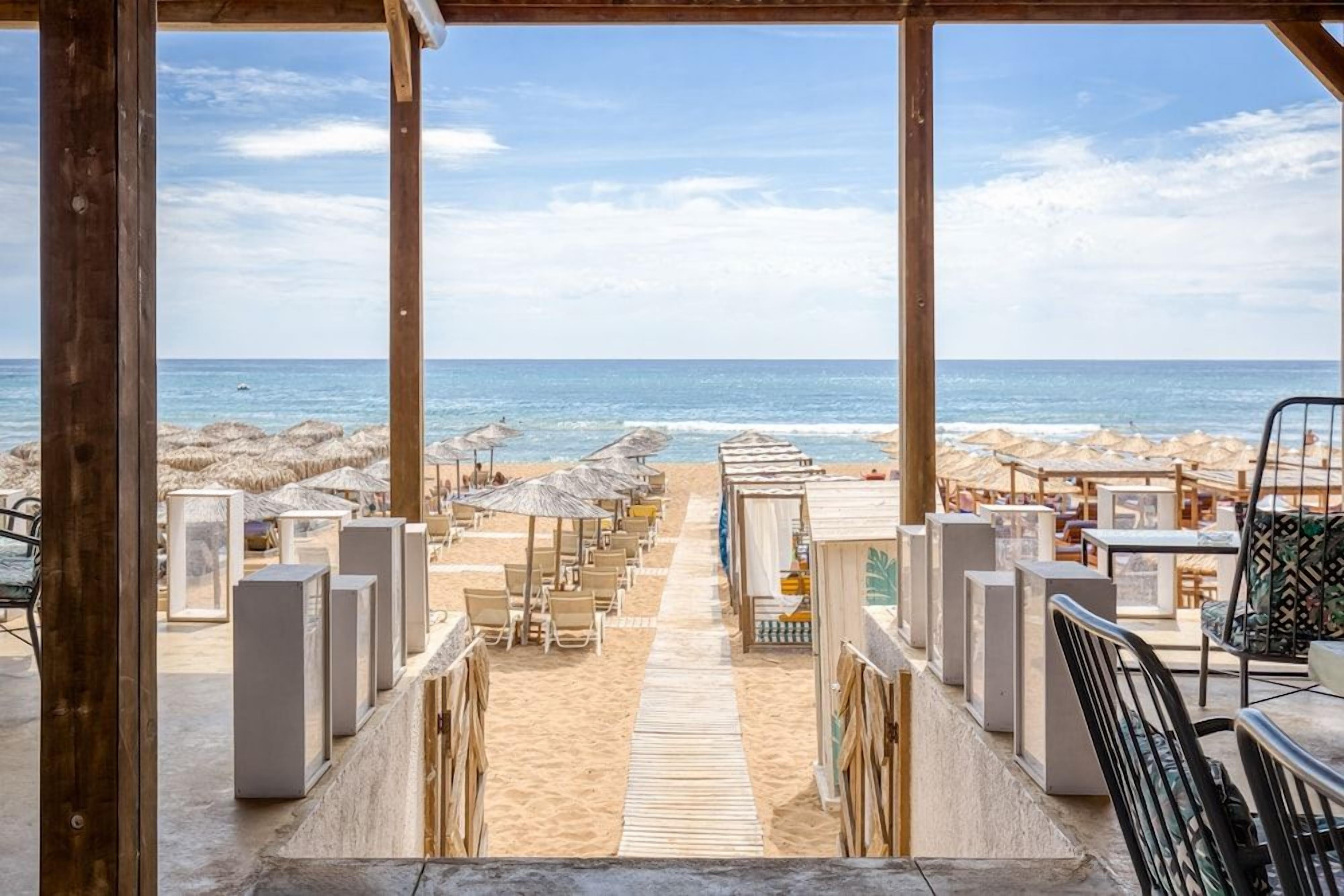 A beachside view with a wooden deck leading to beach umbrellas and seating areas.