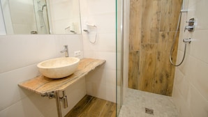 Un baño con lavamanos de piedra, cabina de ducha de vidrio y suelo de madera.