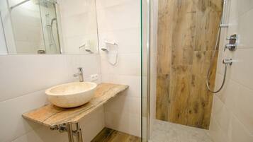 A bathroom with a stone sink, a glass shower enclosure, and wooden flooring.