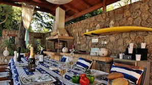 Un espacio de comedor al aire libre con una pared de piedra, una mesa de madera dispuesta con platos, vasos y una botella de vino.