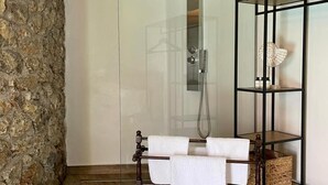 A modern bathroom with a glass shower enclosure, a wooden vanity with a towel rack, and a stone accent wall. - Villa Bournella (Corfu)