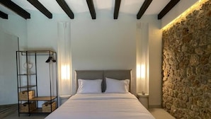 A bedroom with a bed, a ceiling fan, a stone wall, and a metal shelf unit. - Villa Bournella (Corfu)