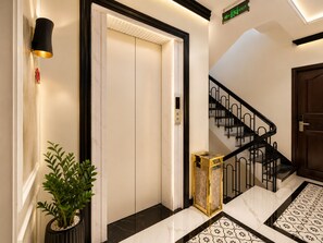 A modern elevator with a digital display, a staircase with black railings, and a potted plant. - KAS Ancient Boutique Hotel (Ben Thanh Ward)