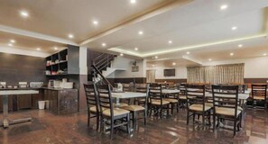 A modern dining area with multiple tables and chairs, a kitchen area with appliances, and a staircase. - OYO Rooms 079 St Marys Hill (Ootacamund)