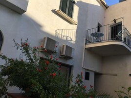 Un edificio con un balcone, condizionatori d'aria e un vaso con fiori rossi.