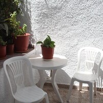Una pequeña mesa redonda con dos sillas de plástico blanco, rodeada de plantas en macetas.