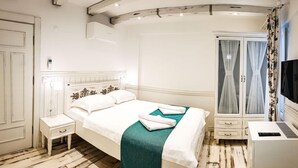 A hotel room with a bed, a bedside table, a desk with a computer, a wardrobe, and a television. - Kalinihta Otel (Bozcaada)