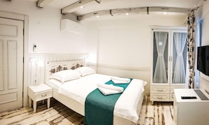 A hotel room with a bed, a bedside table, a desk with a computer, a wardrobe, and a television. - Kalinihta Otel (Bozcaada)