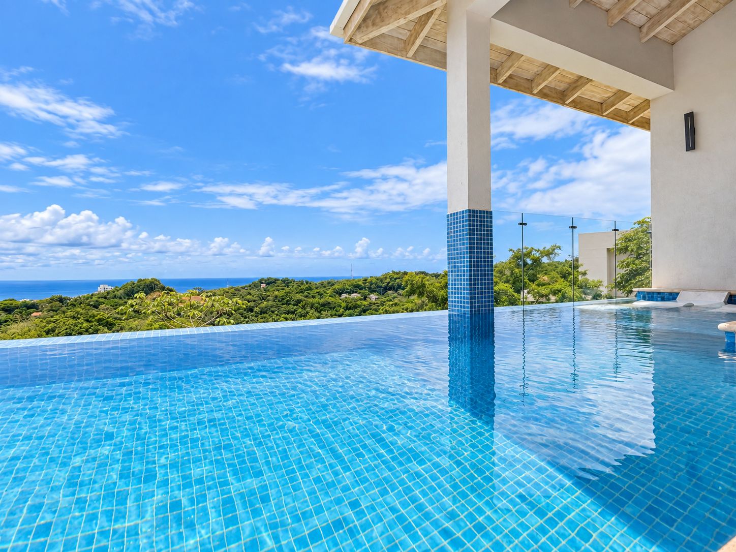A clear blue infinity pool with a view of the ocean and greenery.