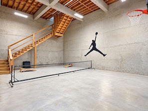 Eine überdachte Basketballhalle mit Netz, einer Holztreppe und einer Betonwand mit der Silhouette eines Basketballspielers.