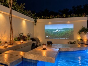 Ein Poolbereich mit integriertem Grill, einer Projektionsleinwand, die einen Film zeigt, und stimmungsvoller Beleuchtung.