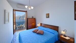 Un dormitorio con cama, cómoda, mesita de noche, lámpara, marco de fotos y vista al mar.