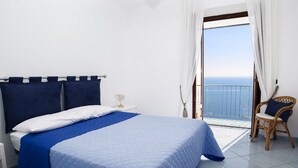 A bedroom with a bed, a nightstand, a chair, and a view of the sea through a balcony. - Moressa Little (Praiano)