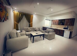 A modern living room with a sofa set, a coffee table, and a kitchen area with cabinets and a microwave. - Tulip Al Rawdah (Riyadh)