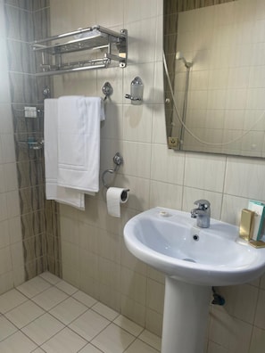 A bathroom with a white sink, a towel rack, a toilet paper holder, and a shower area. - Tulip Al Rawdah (Riyadh)