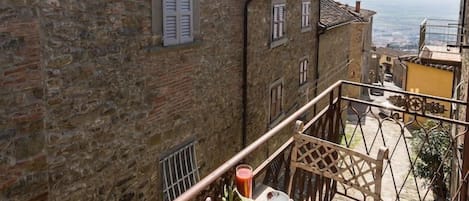 A balcony with a table set for two, overlooking a stone building and a view of the sea.