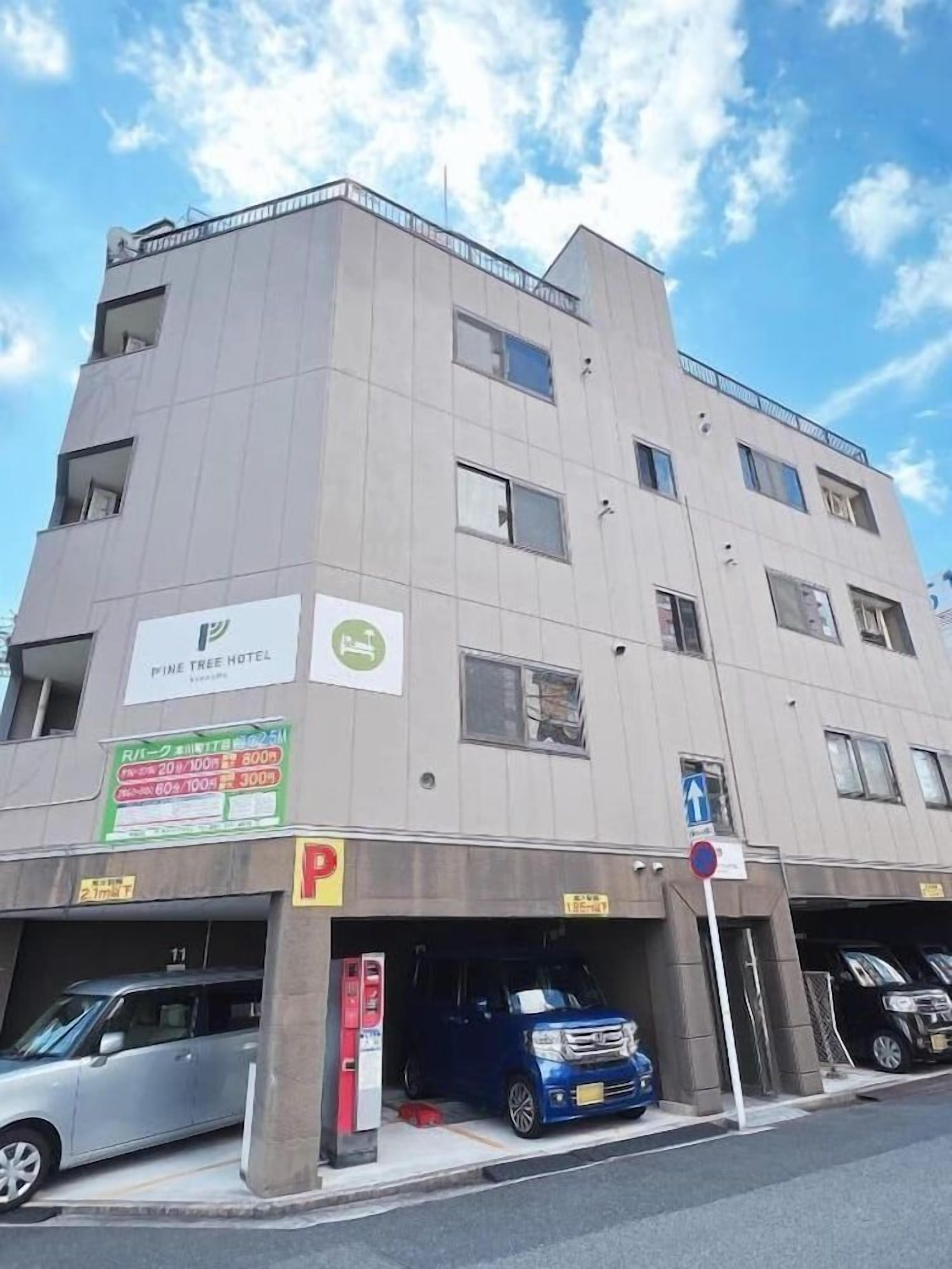 Un hotel de varios pisos con un letrero que dice 'Pine Tree Hotel' y un cartel de estacionamiento que indica una distancia de 300 metros al hotel.