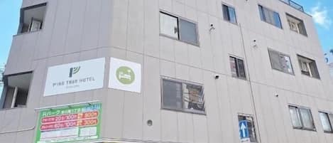 Un hotel de varios pisos con un letrero que dice 'Pine Tree Hotel' y un cartel de estacionamiento que indica una distancia de 300 metros al hotel.