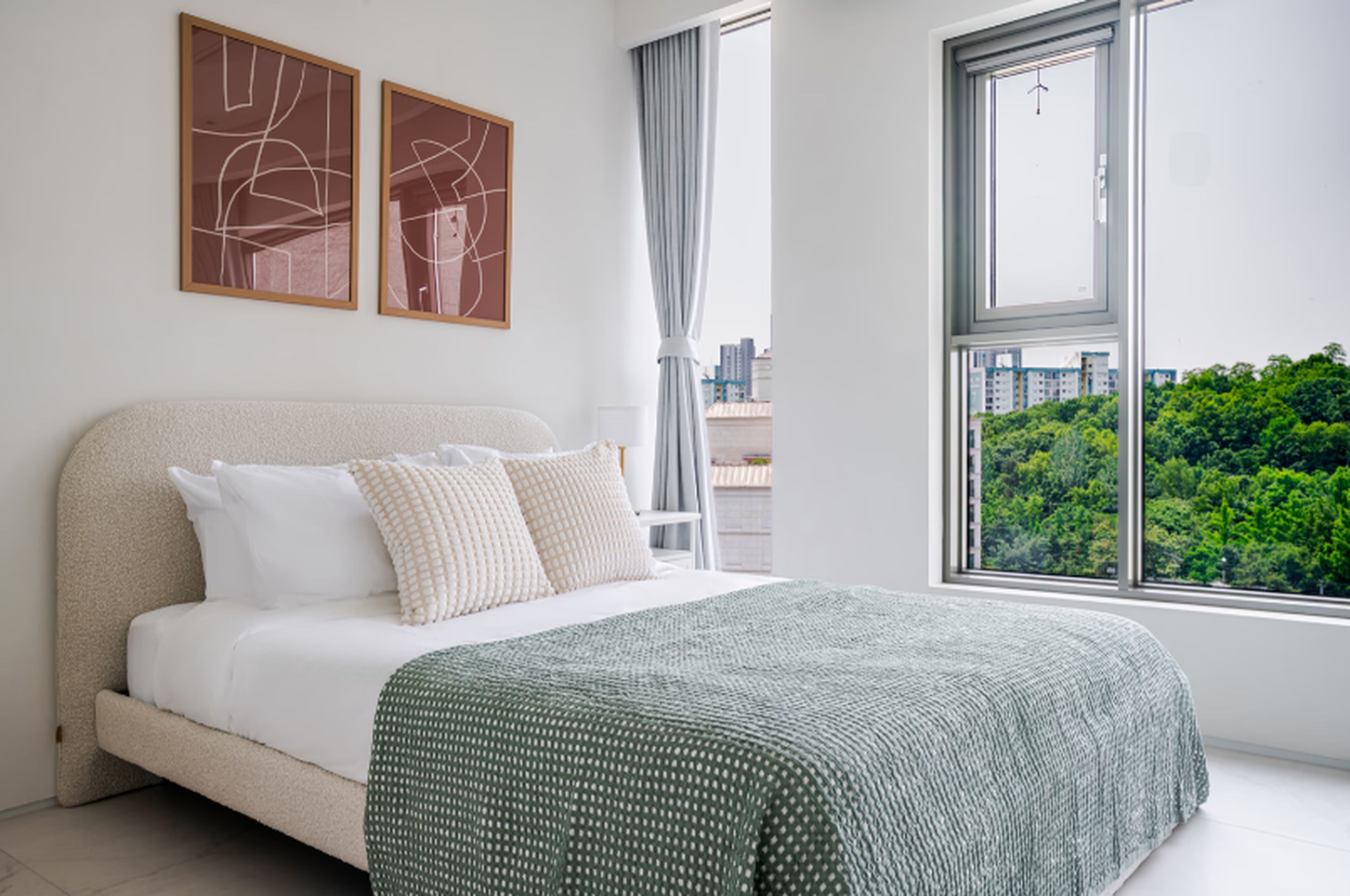 Un dormitorio moderno con una cama grande, dos pinturas abstractas, vistas de un paisaje urbano y una ventana con cortinas.