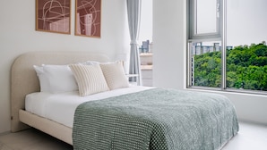 A modern bedroom with a large bed, two abstract paintings, a view of a cityscape, and a window with curtains. - Orchid Cheongdam - Executive Suite - 5 mins to Coex by Taxi (Seoul)