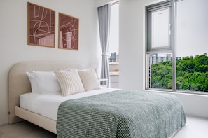 Un dormitorio moderno con una cama grande, dos pinturas abstractas, vistas de un paisaje urbano y una ventana con cortinas.