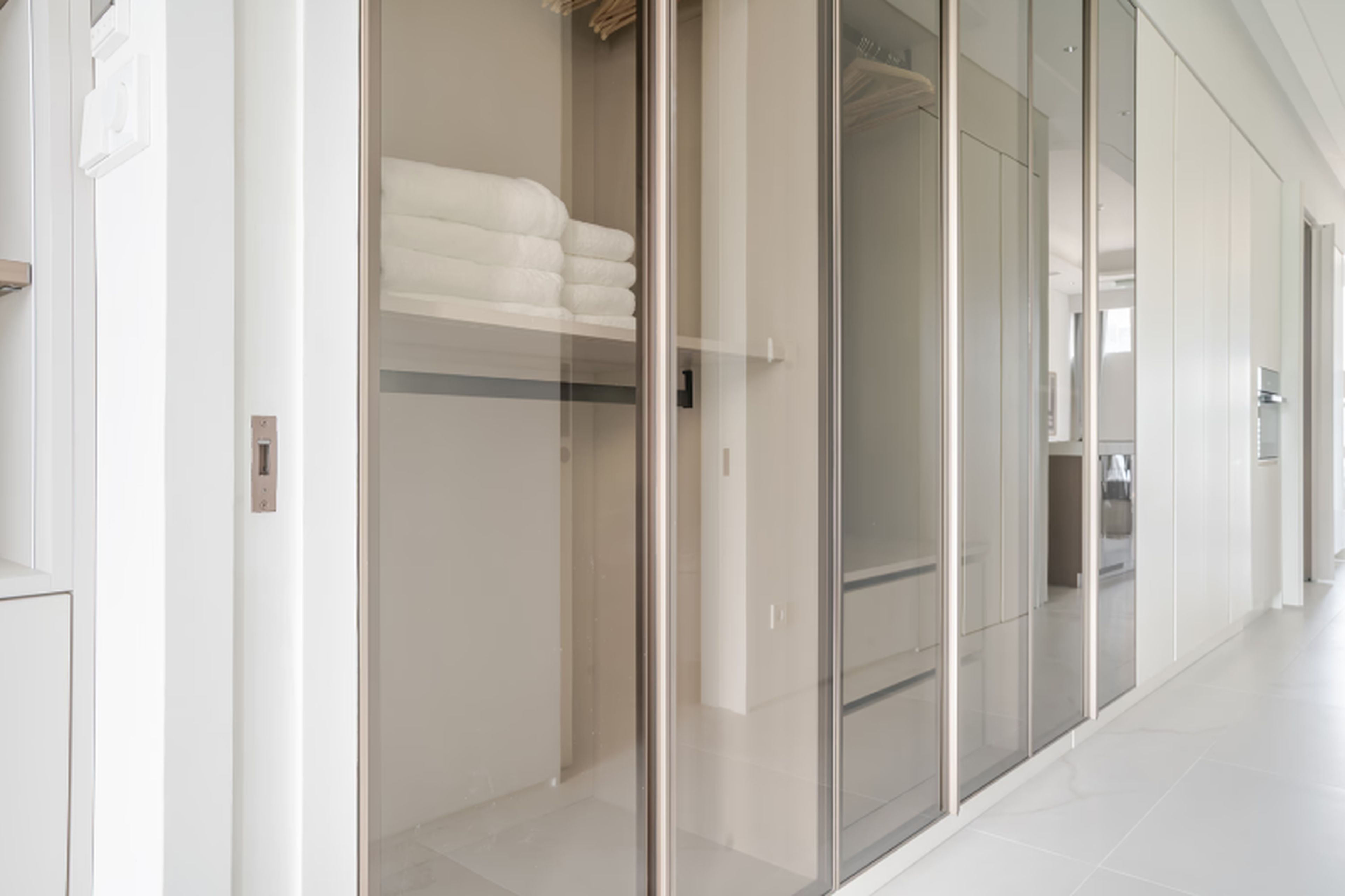 A modern hotel corridor with a glass door leading to a room with a bed and a neatly folded white towel.
