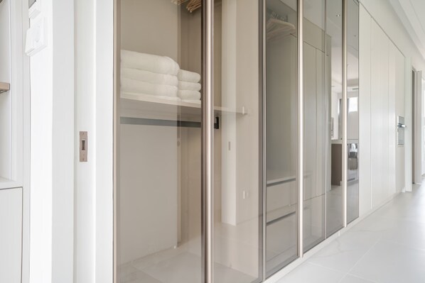 A modern hotel corridor with a glass door leading to a room with a bed and a neatly folded white towel.