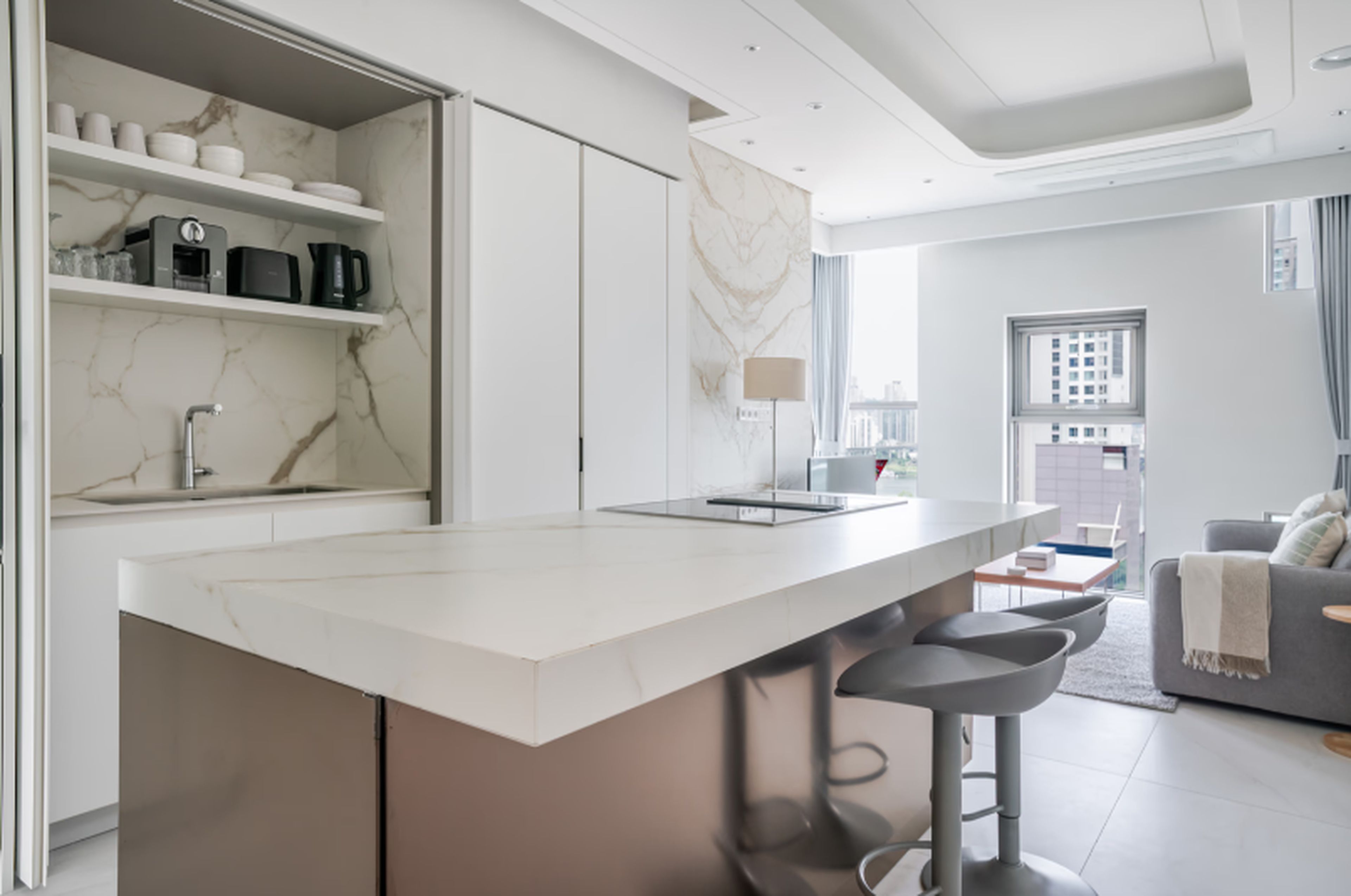 A modern kitchen with a marble countertop, built-in appliances, and a large window.