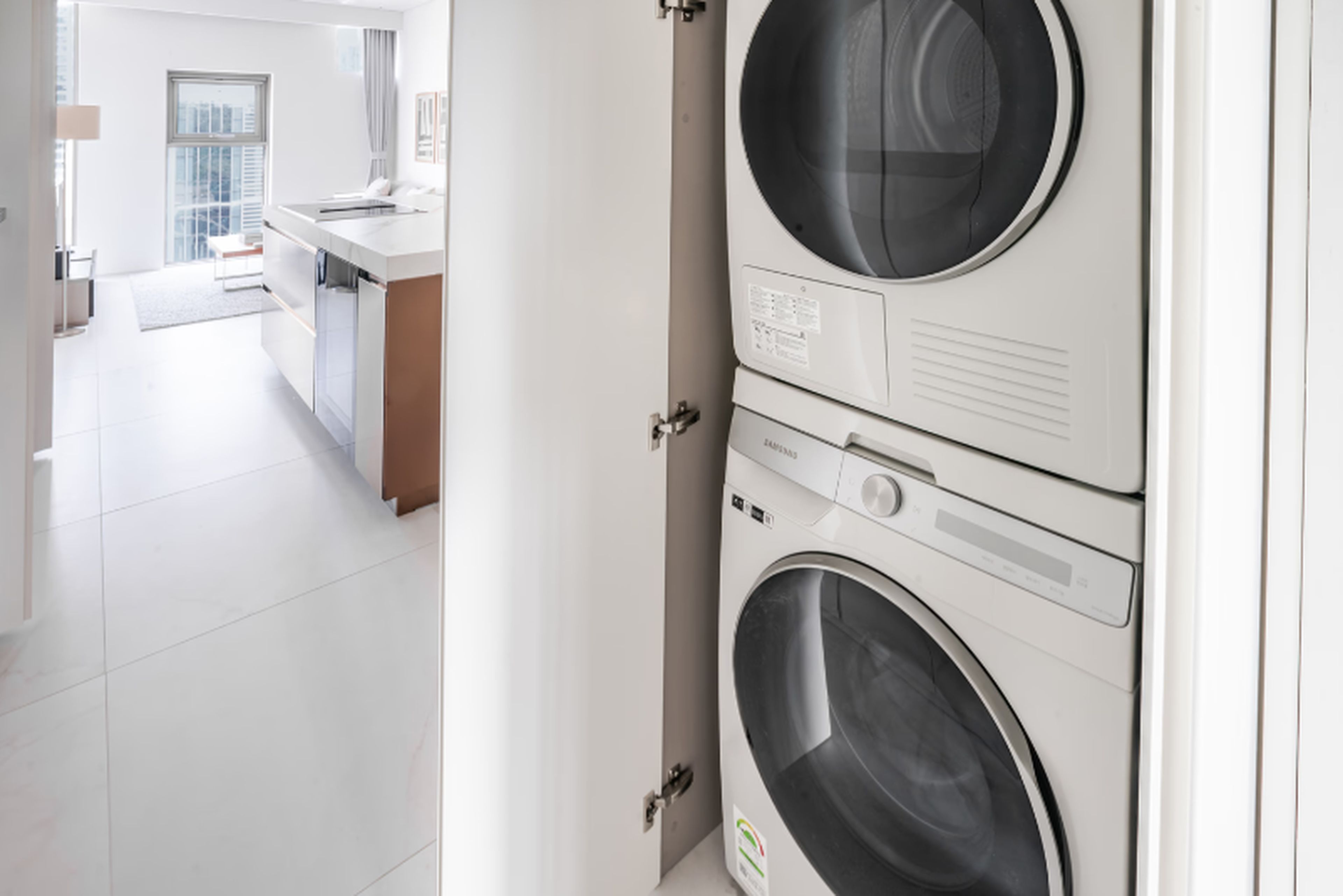 A modern laundry room with stacked washing machines and a view into a contemporary kitchen area.