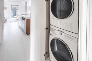 A modern laundry room with stacked washing machines and a view into a contemporary kitchen area.