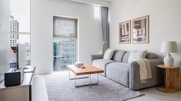 A modern living room with a grey sofa, a coffee table, and a city view through large windows.