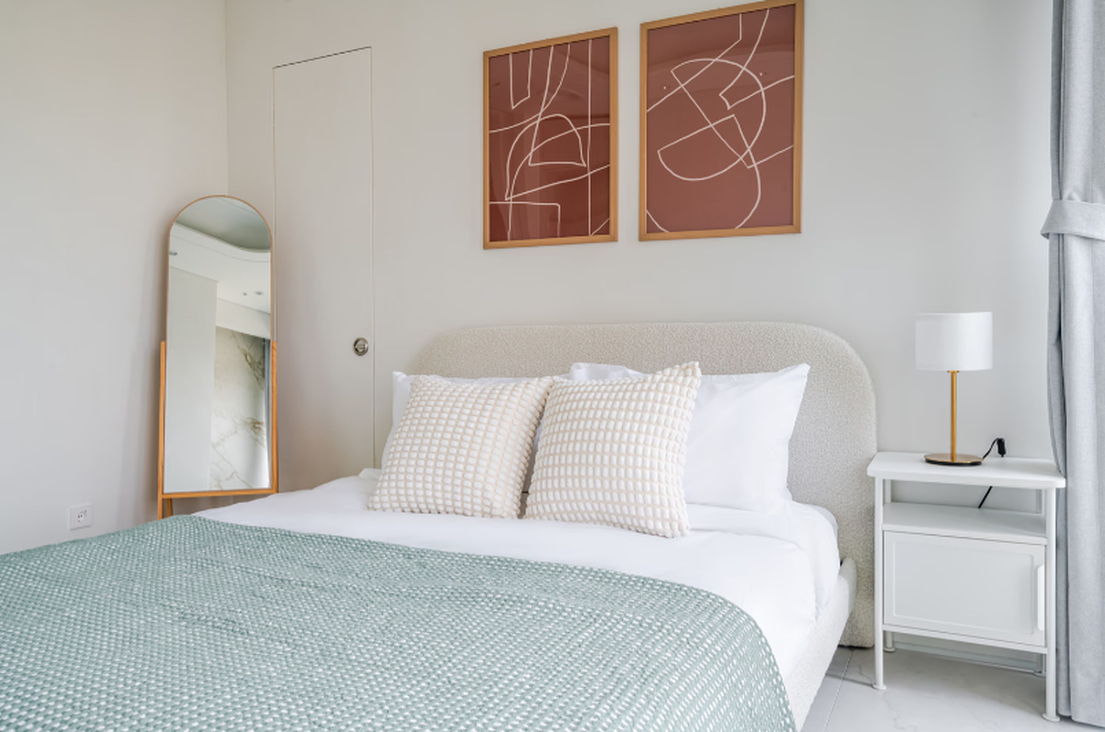 A hotel room with a bed, a nightstand, a lamp, and abstract artwork on the wall.