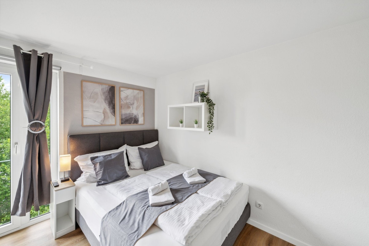 Ein modernes Schlafzimmer mit einem Bett, Nachttischen, einem Fenster mit Vorhängen und Wanddekoration.