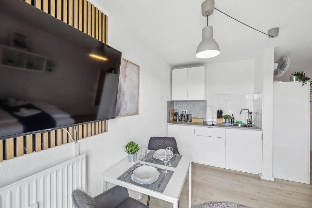Eine moderne Küche mit weißen Schränken, ein Essbereich mit Tisch für Zwei und ein an der Wand montierter Fernseher.