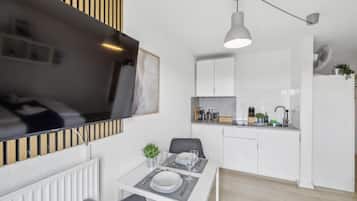 Een moderne keuken met witte kasten, een eethoek met een tafel gedekt voor twee personen en een aan de muur bevestigde televisie.