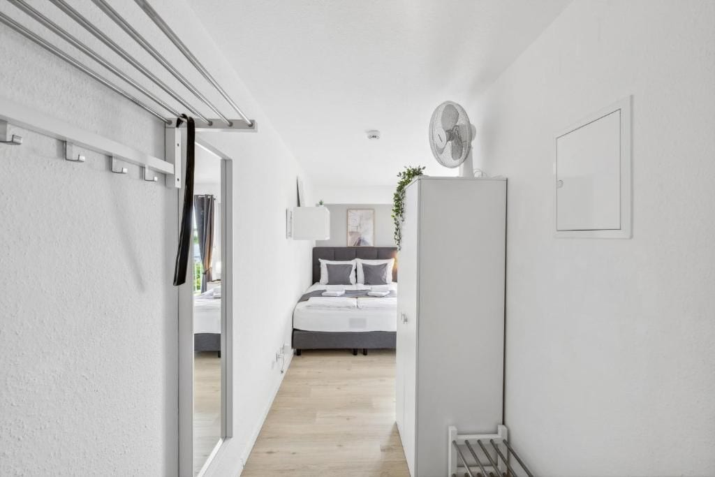 Un dormitorio moderno con cama, mesita de noche, ventilador de pared y una puerta que da a otra habitación.