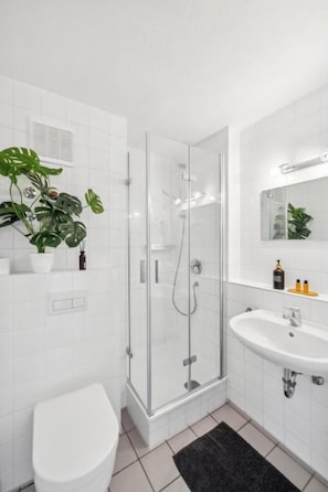 Ein modernes Badezimmer mit einer in Glas abgeschirmten Dusche, einem weißen Waschbecken und einer Toilette.
