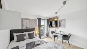 Habitación de hotel moderna con cama, escritorio, silla, televisor montado en la pared y vistas al exterior.