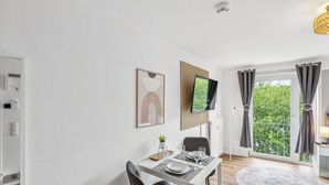 Un comedor moderno con una mesa blanca, sillas y un televisor de pantalla plana montado en la pared.