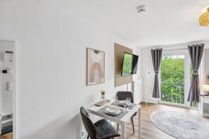 Ein moderner Essbereich mit einem weißen Tisch, Stühlen und einem an der Wand befestigten Flachbildfernseher.