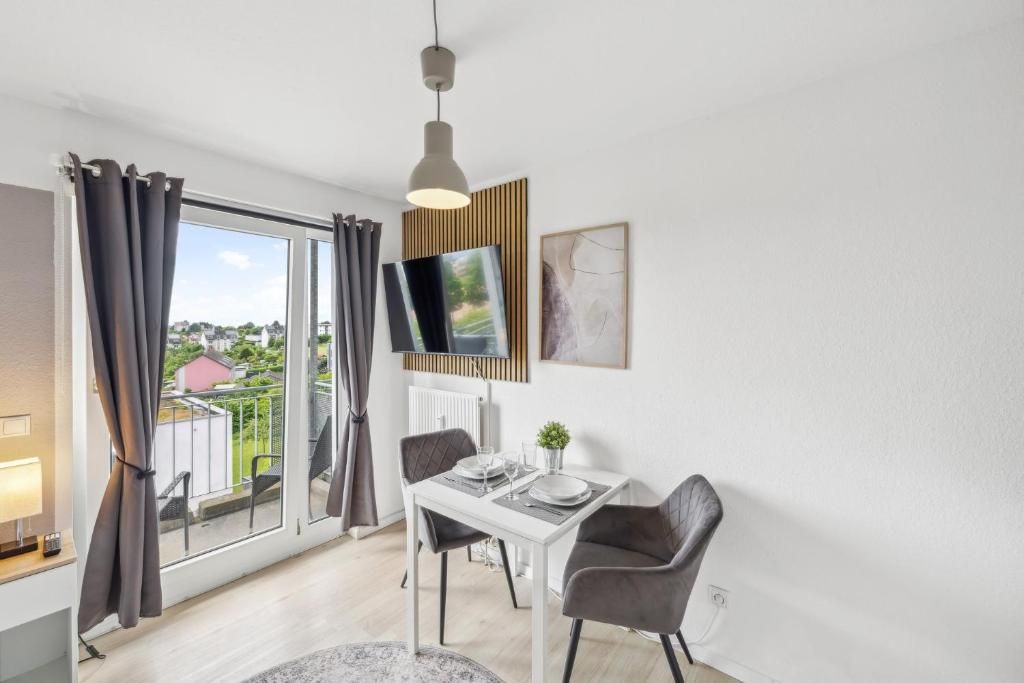 Ein moderner Essbereich mit einem Tisch für zwei Personen, einem an der Wand befestigten Fernseher und Blick ins Freie durch große Fenster.