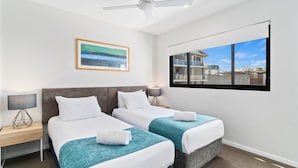 A hotel room with two beds, a ceiling fan, a painting, a window with a view, and a nightstand with a lamp. - Sea Breeze Mooloolaba (Sunshine Coast)