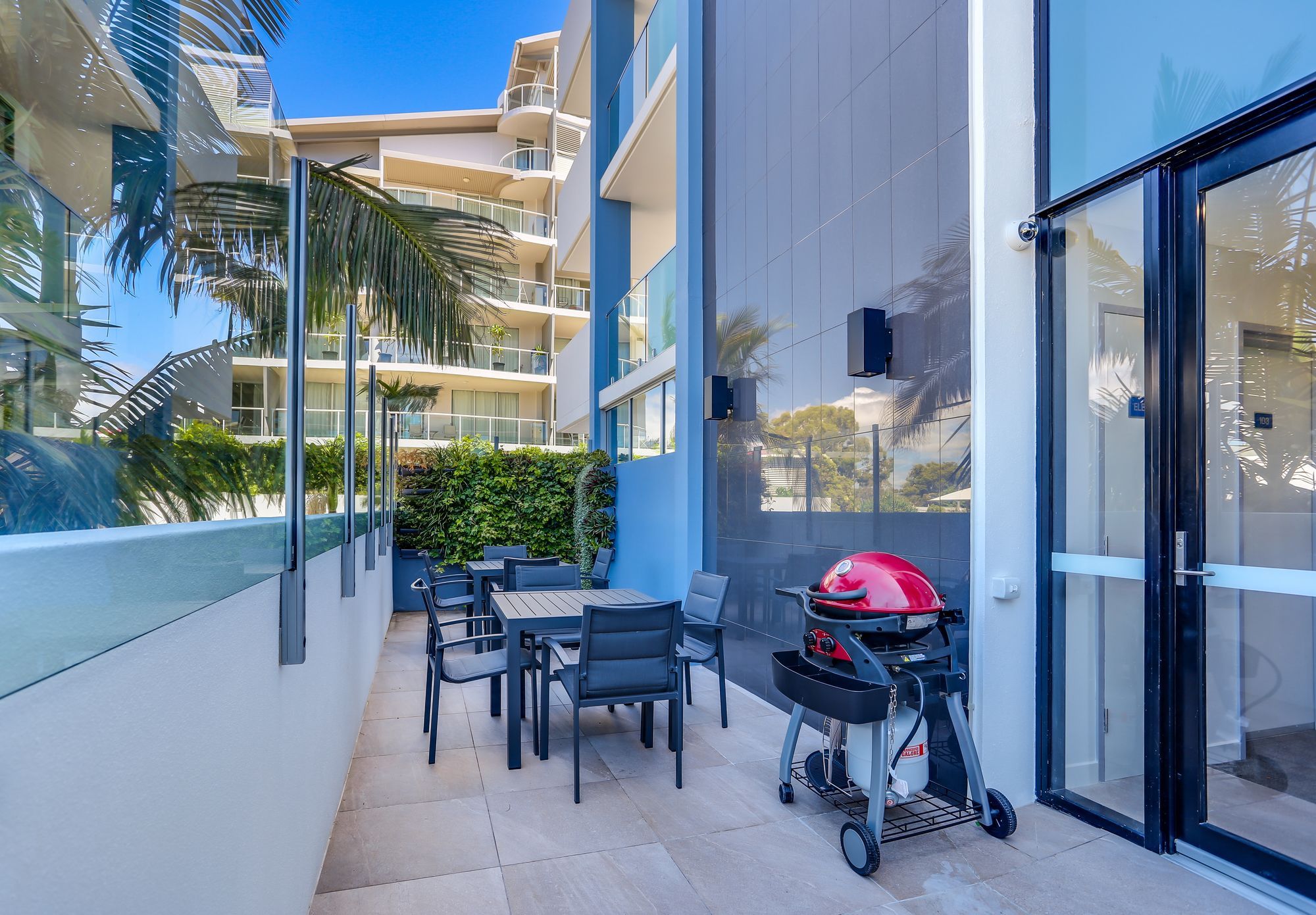 A balcony with outdoor furniture, a barbecue grill, and a view of a multi-story building.