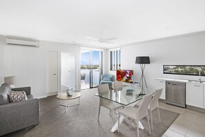 Um apartamento moderno com mesa de jantar de vidro, sofá, cozinha equipada com lava-louças e varanda com vista.