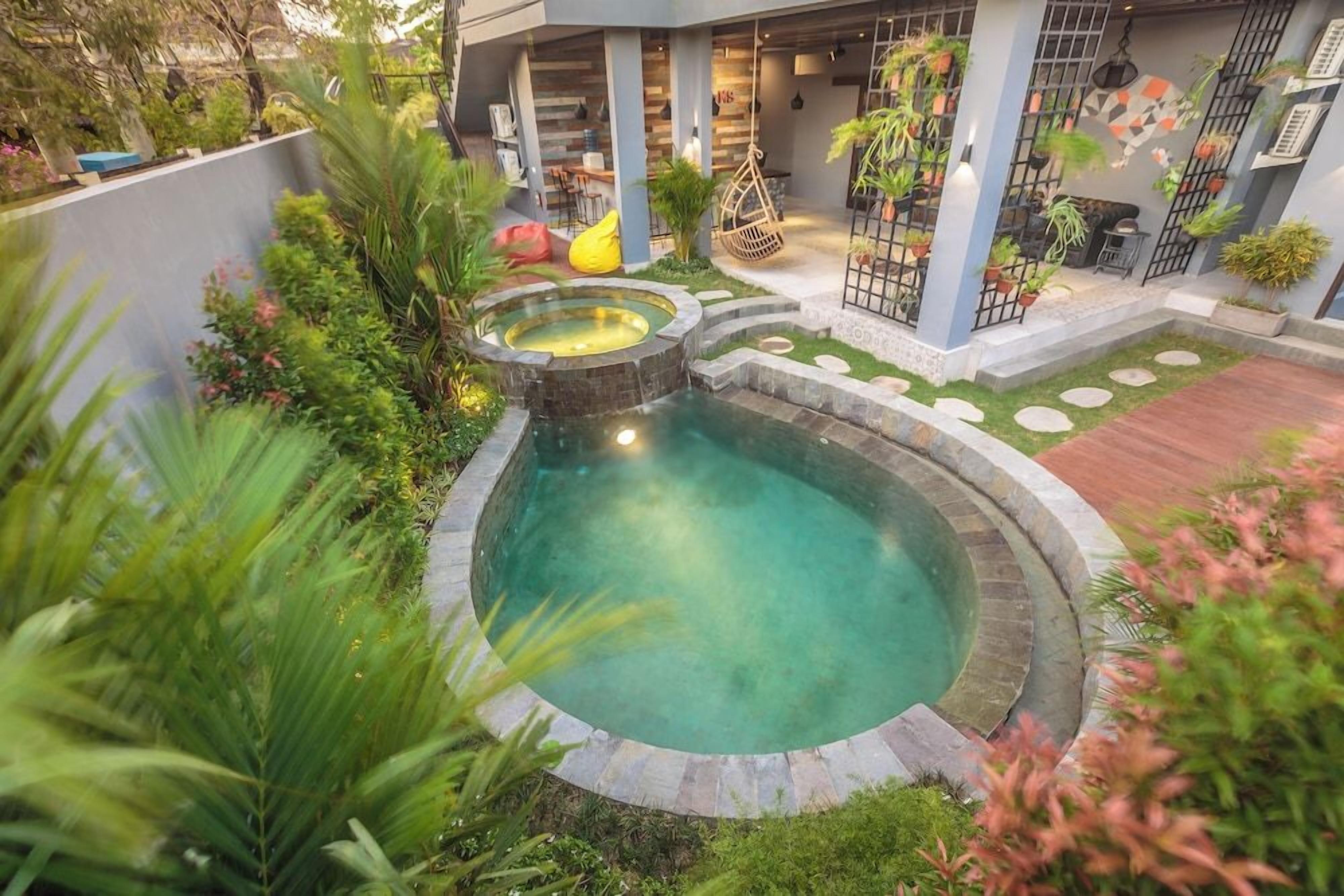 A circular pool with a stone edge, surrounded by lush greenery and a small garden area.