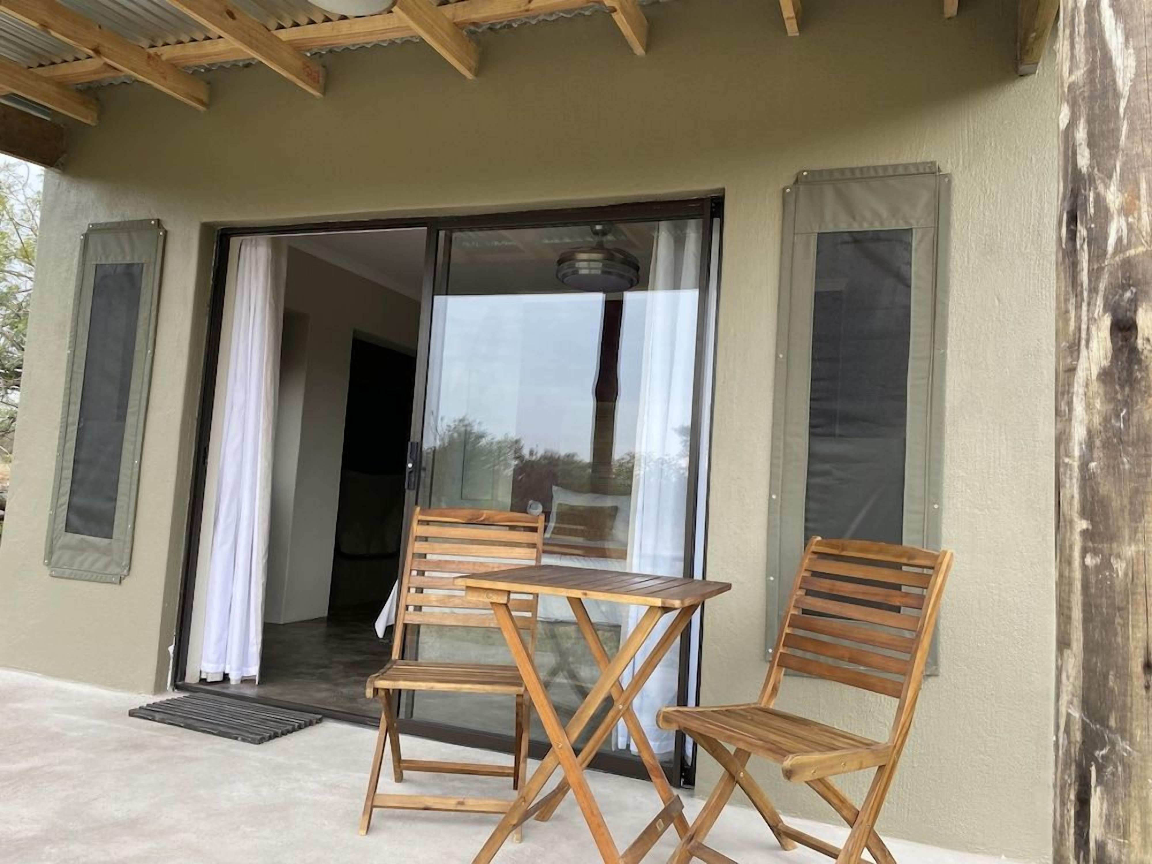 Un espacio al aire libre techado con una mesa, dos sillas, un ventanal corredero y un poste de madera.