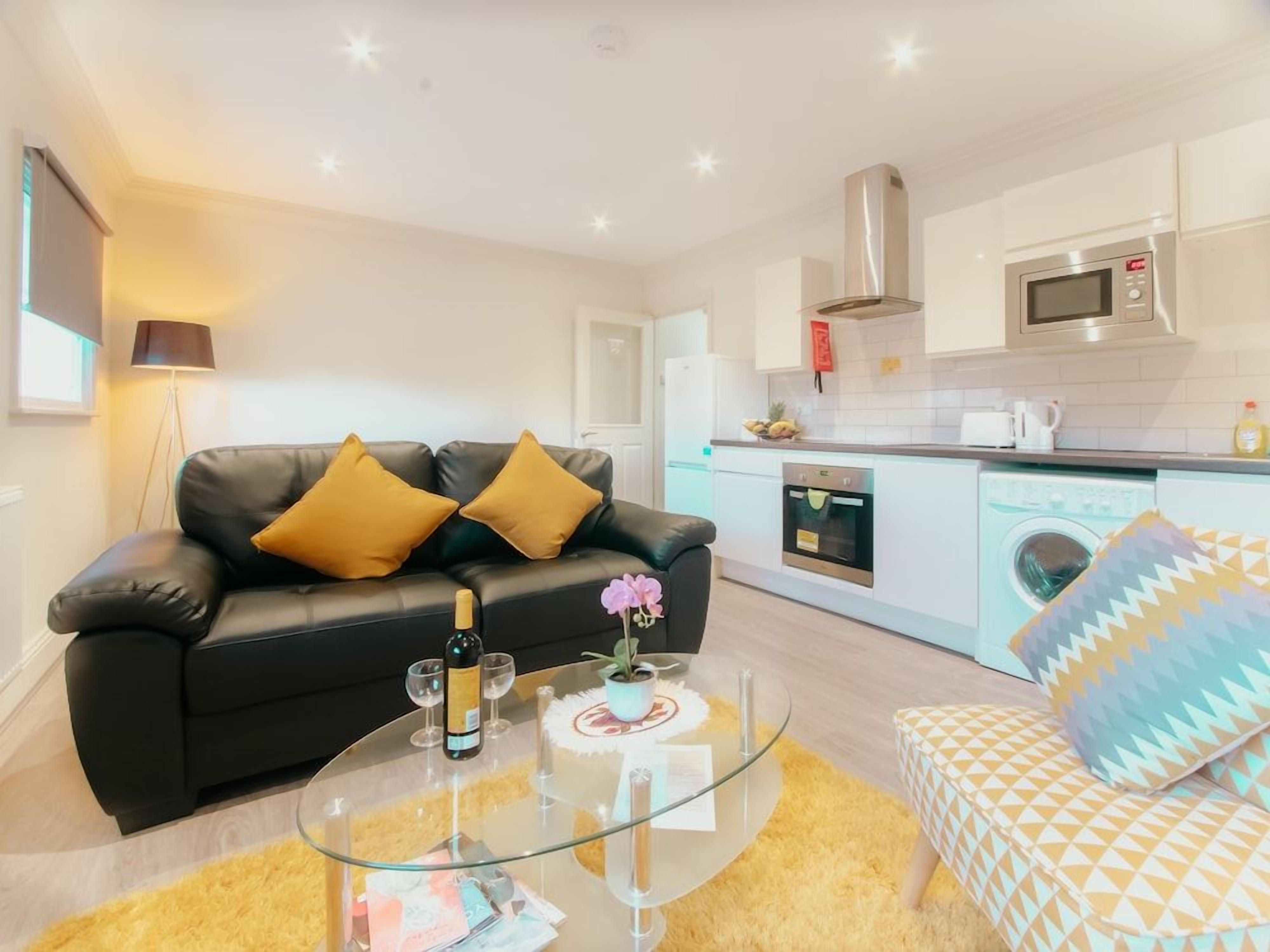 A modern living room with a black leather sofa, a glass coffee table, and a yellow rug.