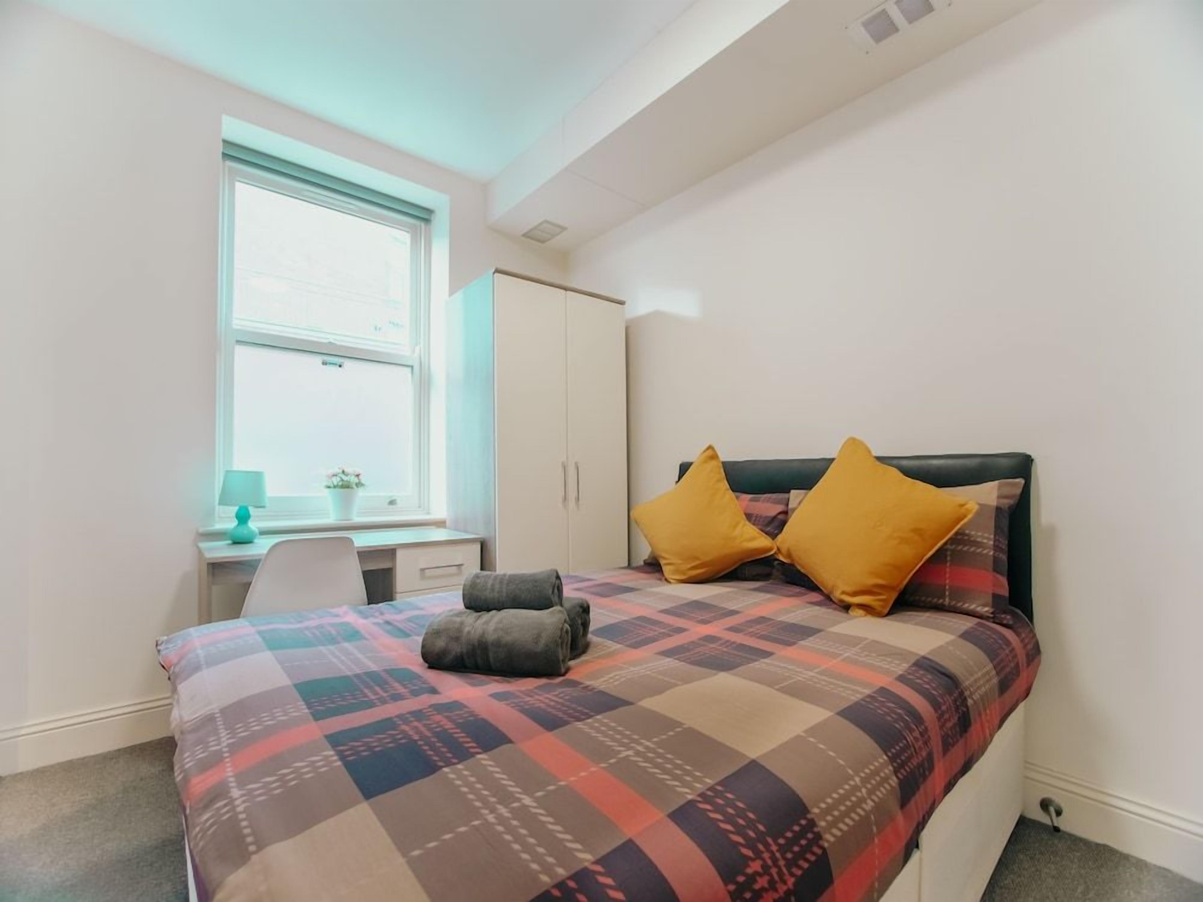 A bedroom with a bed, a desk, and a window.