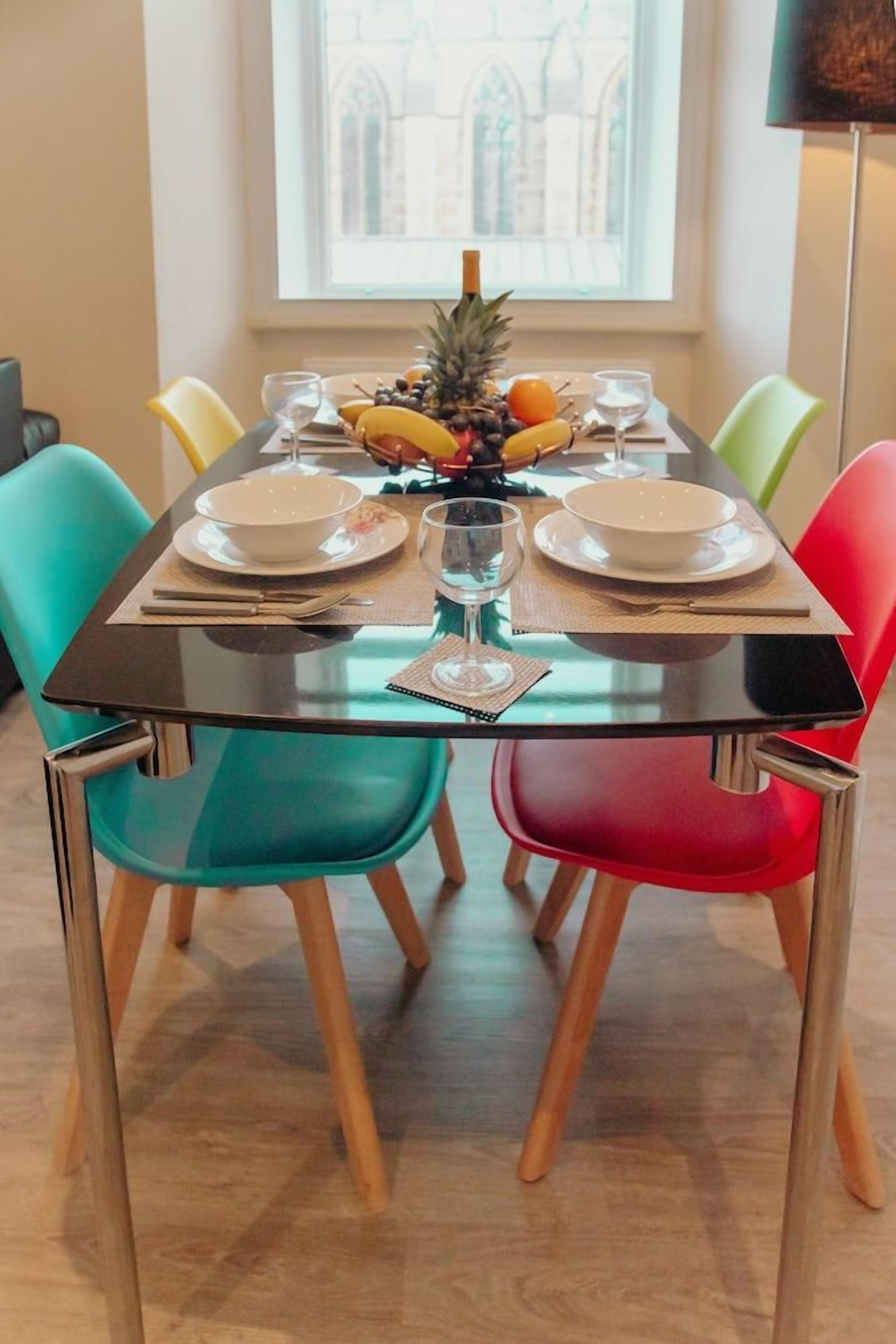 A dining table set with plates, bowls, and a centerpiece of fruit and a bottle.
