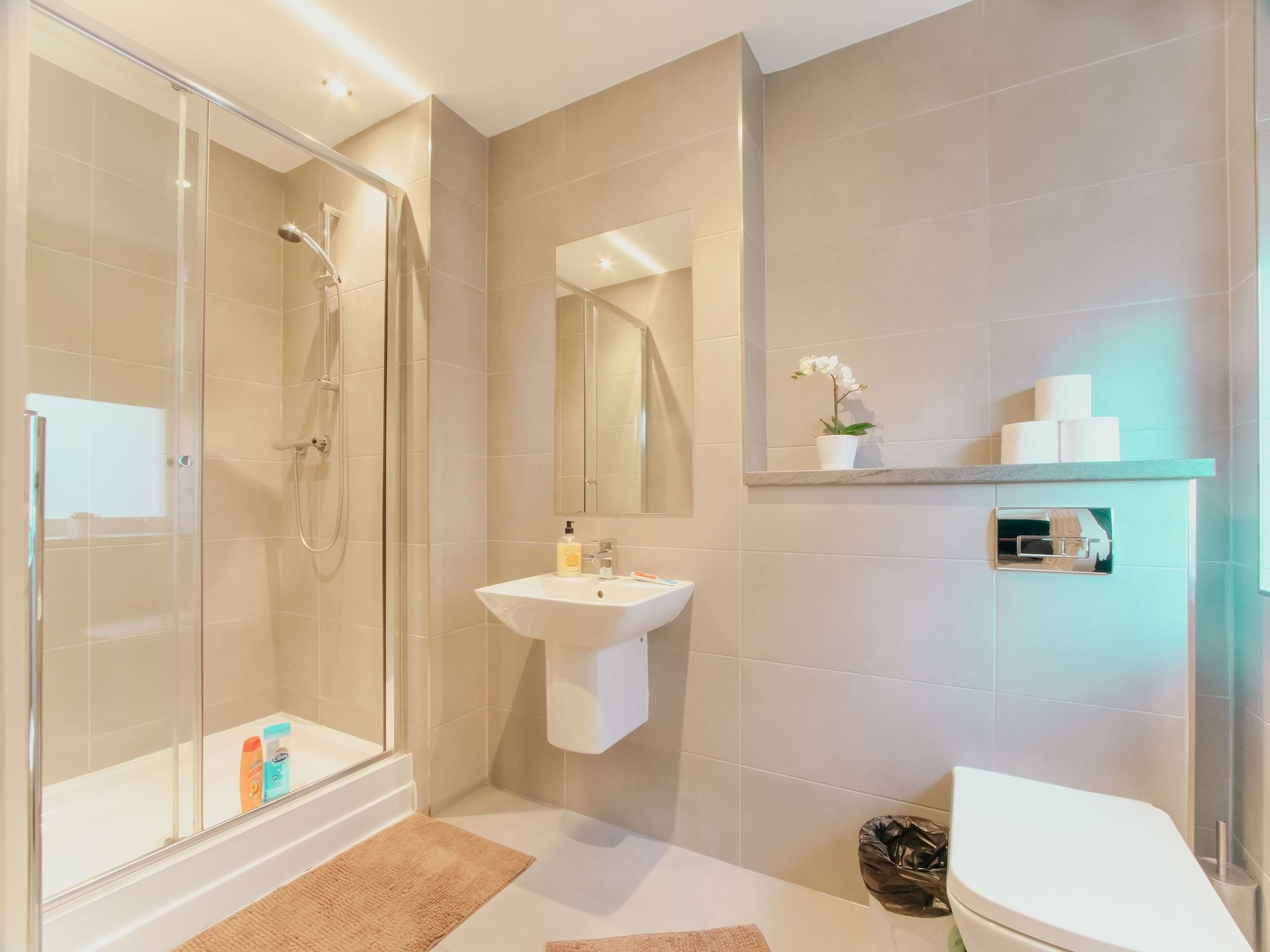 A modern bathroom with a glass-enclosed shower, a pedestal sink, and a toilet.
